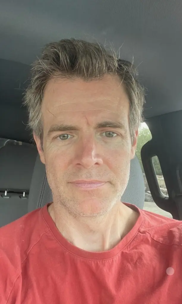Phil Milne in the driver's seat of a vehicle, wearing a red shirt.